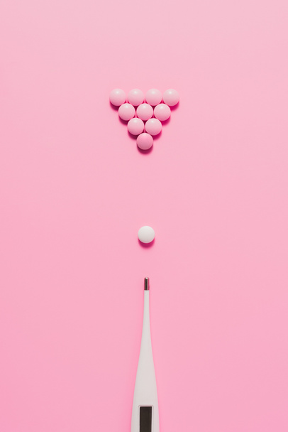 vista superior de pílulas com termômetro elétrico dispostos em composição de bilhar em rosa
 - Foto, Imagem