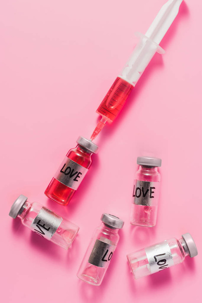 top view of syringe and bottles with love vaccine signs on pink tabletop - Foto, Imagem