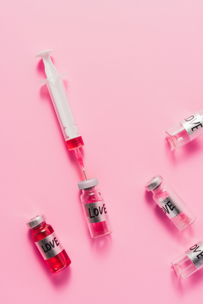 top view of syringe and bottles with love vaccine signs on pink surface - Photo, Image