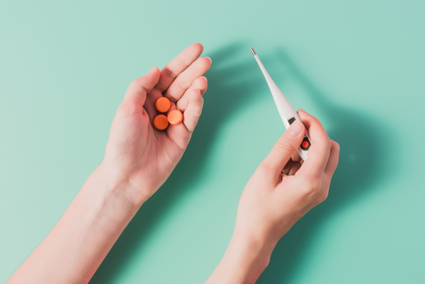 cropped shot of woman holding heap of pills and thermometer on blue - Photo, Image