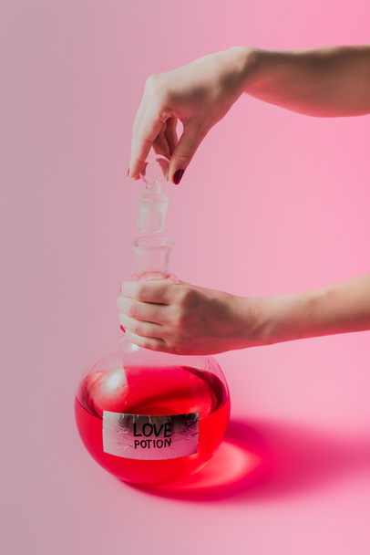 cropped shot of woman opening flask with red colored love potion on pink surface - 写真・画像