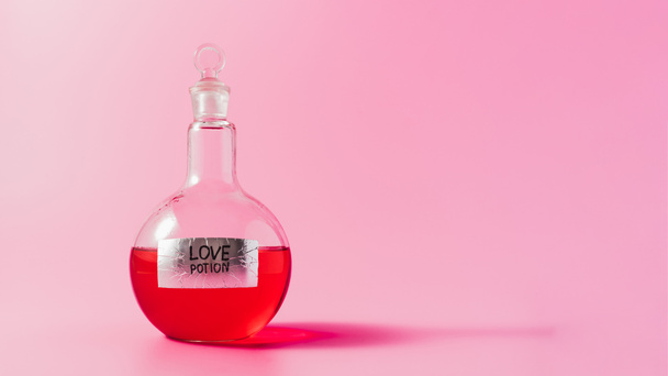 close-up shot of flask with red colored love potion on pink surface - Фото, изображение