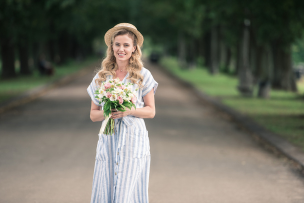 lovely woman in trendy trendy posing with bouquet of flowers on path in park - Foto, afbeelding