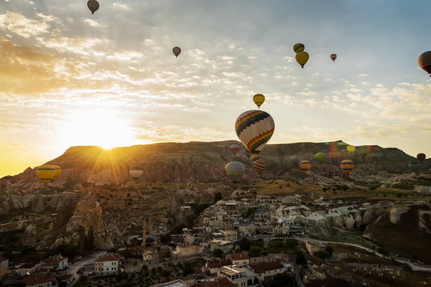 Balloons flying over the ancient cave city at dawn. The sun is coming out from behind the mountain. Fantastic area and balloons. Turkey. Cappadocia. Goreme National Park. - Foto, Bild