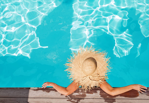 Woman in big straw hat sitting in the swimming pool - Foto, afbeelding
