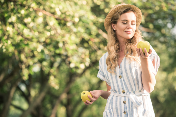 hasır şapka elinde iki elma ile poz mutlu sarışın kadın - Fotoğraf, Görsel
