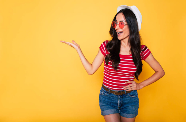 young brunette woman in white hat and glasses posing on yellow background  - Photo, image
