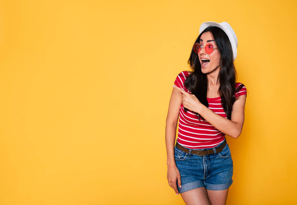 young brunette woman in white hat and glasses posing on yellow background  - 写真・画像