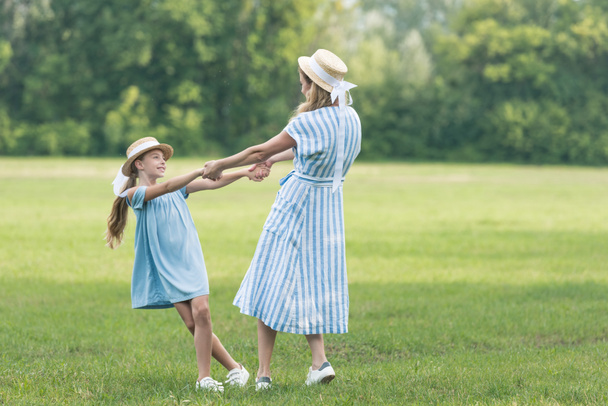 Mutter und Tochter halten Händchen, drehen sich und haben Spaß auf grünem Rasen  - Foto, Bild