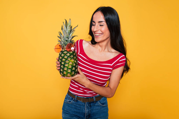 young brunette woman posing with pineapple on yellow background  - Foto, Imagen