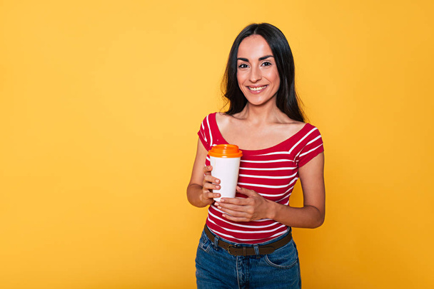 young brunette woman posing with paper coffee cup on yellow background  - Foto, Imagem