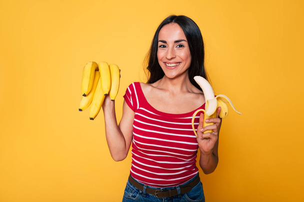 young brunette woman posing with bananas on yellow background  - Zdjęcie, obraz
