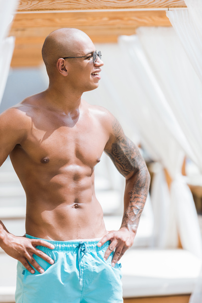 shirtless tattooed muscular man standing near sun loungers and looking away - Foto, imagen