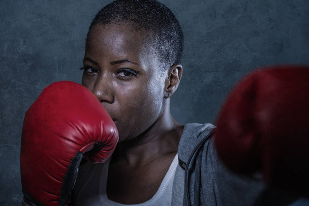 close up face portrait of young angry and defiant black afro American sport woman in boxing gloves training and posing as a dangerous fighter in fitness gym and fight workout concept - 写真・画像
