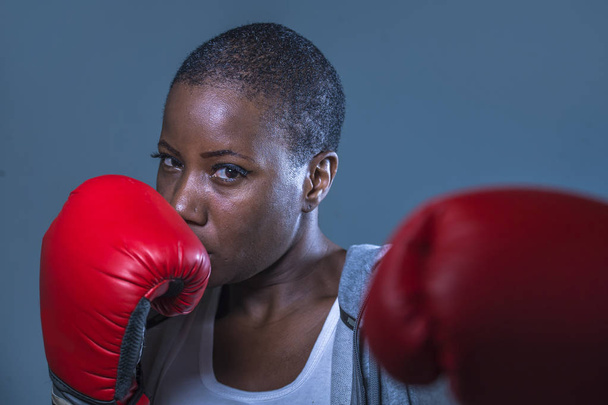 close up face portrait of young angry and defiant black afro American sport woman in boxing gloves training and posing as a dangerous fighter in fitness gym and fight workout concept - 写真・画像