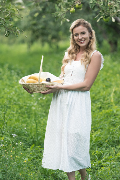 緑果樹園の果物の枝編み細工品バスケットを持って幸せな女 - 写真・画像