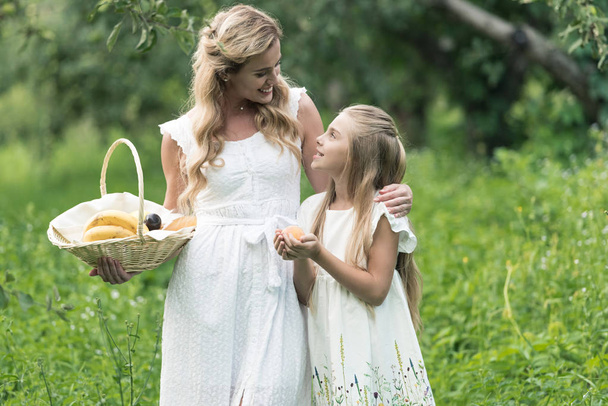 adorable daughter and mother holding wicker basket with fruits - Photo, Image