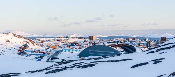 Lotes de casas Inuit espalhadas na colina na cidade de Nuuk coberto de neve com fiorde do mar e montanhas no fundo, Groenlândia
 - Foto, Imagem