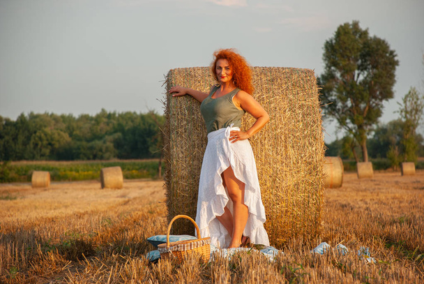 Рыжая женщина позирует на поле возле стога сена
 - Фото, изображение