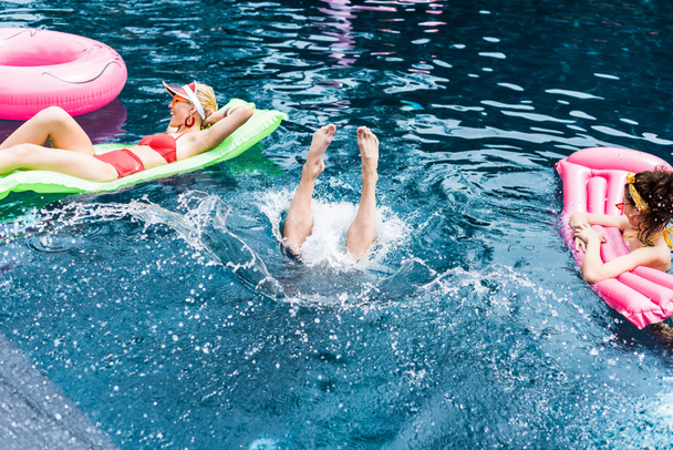 αρσενικό πόδια να κολλήσει έξω από το νερό ανάμεσα σε δύο γυναίκες φίλους σε Φουσκωτά στρώματα στην πισίνα - Φωτογραφία, εικόνα