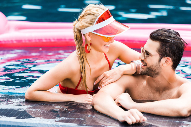 young couple in sunglasses looking at each other near poolside  - Photo, Image