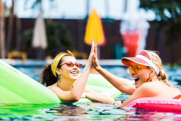 souriant amis féminins avec matelas gonflables prenant haute cinq dans la piscine
  - Photo, image