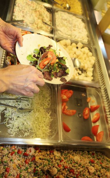 hand van de bediende tijdens de lunchpauze dat de plaat met verse sla en gele mais voor een lunchpauze vegan vult - Foto, afbeelding