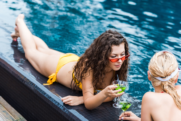 young female friends resting on poolside with green cocktails  - Fotoğraf, Görsel