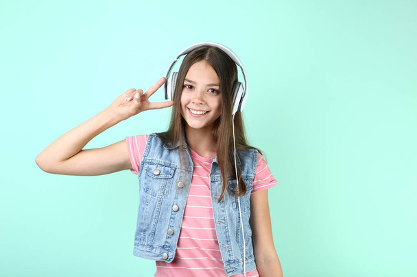 Young girl listening to music on headphones and showing peace symbol on mint background - Foto, imagen