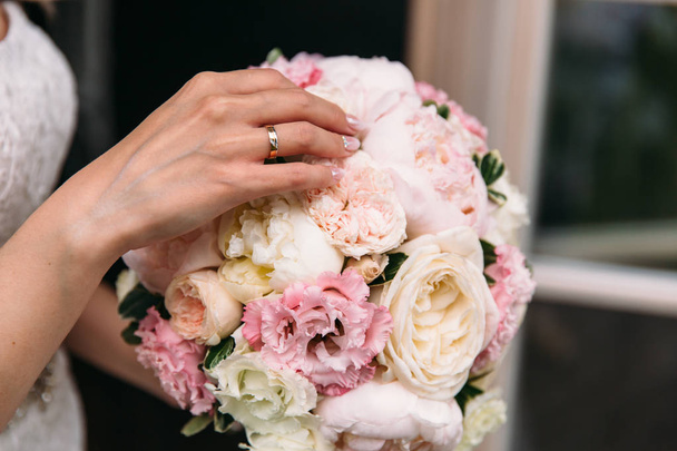 Close-up of a cropped frame, the hand of a young girl with an engagement ring on a ring finger. Gently touches the wedding bouquet of peonies. Wedding day, bouquet of the bride. wedding ring - Foto, afbeelding