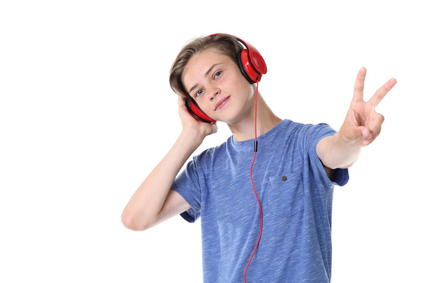 Cute teenager boy listening to music on headphones and  showing peace symbol on white background - Φωτογραφία, εικόνα