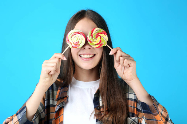 Young girl with holding lollipops in front of her eyes on blue background - Фото, зображення