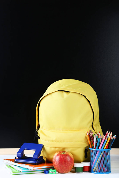 Yellow backpack with school supplies on black background - Foto, afbeelding