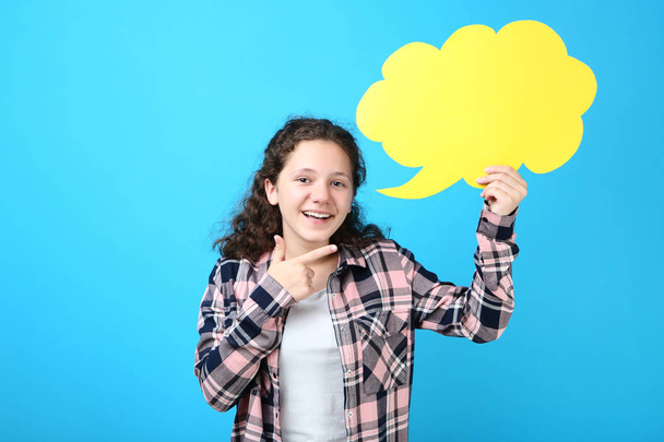 Young girl holding speech bubble and pointing finger aside on blue background - Foto, afbeelding