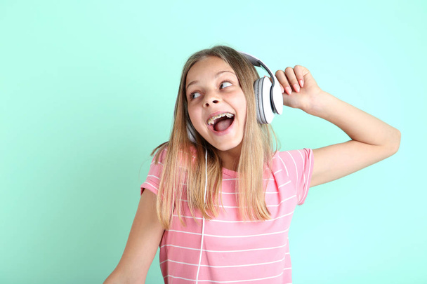 Beautiful teenager girl listening to music on headphones on mint background - Foto, imagen