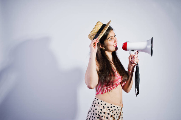 Portrait of a gorgeous young girl in swimming suit and hat talks into megaphone in studio. - 写真・画像