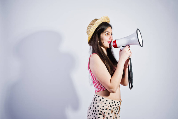 Portrait of a gorgeous young girl in swimming suit and hat talks into megaphone in studio. - Foto, Imagem
