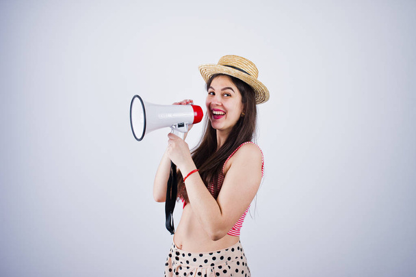 Portrait of a gorgeous young girl in swimming suit and hat talks into megaphone in studio. - Foto, imagen