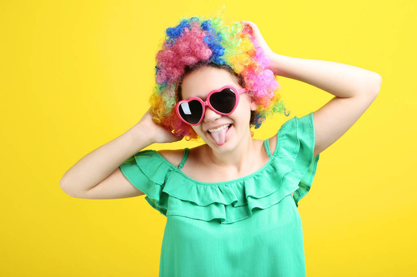 girl in clown wig and sunglasses showing tongue out on yellow background - Photo, image