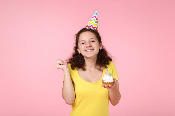 Beautiful happy in birthday cap holding cupcake on pink background - Valokuva, kuva