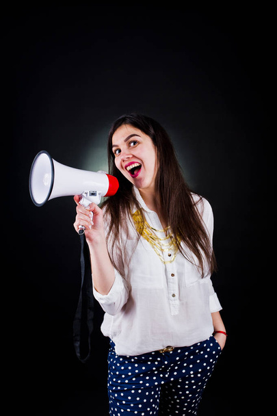 Portrait of a young woman in blue trousers and white blouse posing with megaphone in the studio. - Photo, Image