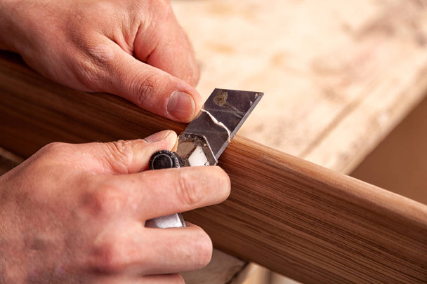 Γκρο πλαν Α ξυλουργός με ρούχα εργασίας αποκαθιστώντας ένα ξύλο με μια σπάτουλα σε ένα ξύλινο τραπέζι. Ξύλινα μπλοκ σοβατίσματος εργαζόμενος κατασκευή άνθρωπος - Φωτογραφία, εικόνα