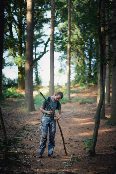 Подросток в лесу режет ветку ножом.
. - Фото, изображение