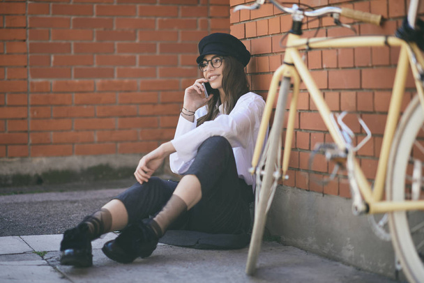 Femme assise sur le trottoir et utilisant un téléphone intelligent. À côté de son vélo jaune
. - Photo, image