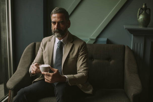 Πορτρέτο του όμορφος ανώτερος επιχειρηματίας που πίνει καφέ στο λόμπι - Φωτογραφία, εικόνα