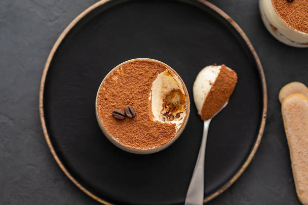 Heerlijk Italiaans dessert tiramisu, chocolade, cacao en koffie bonen op een zwarte achtergrond. Bovenaanzicht met kopie ruimte. - Foto, afbeelding