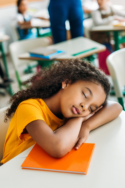 moe Afro-Amerikaanse schoolmeisje slapen op Bureau tijdens de les - Foto, afbeelding