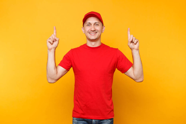 Zusteller in roter Uniform isoliert auf gelb-orangefarbenem Hintergrund. Professionell lächelnder männlicher Angestellter mit Schirmmütze, T-Shirt, das als Kurierfahrer arbeitet und Zeigefinger auf Kopierfläche zeigt. Dienstleistungskonzept - Foto, Bild