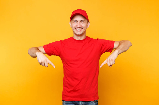 Delivery man in red uniform isolated on yellow orange background. Professional smiling male employee in cap, t-shirt working as courier dealer pointing index fingers down copy space. Service concept - Fotografie, Obrázek