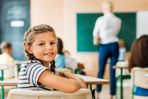 adorable little schoolgirl looking at camera during lesson - Foto, Bild